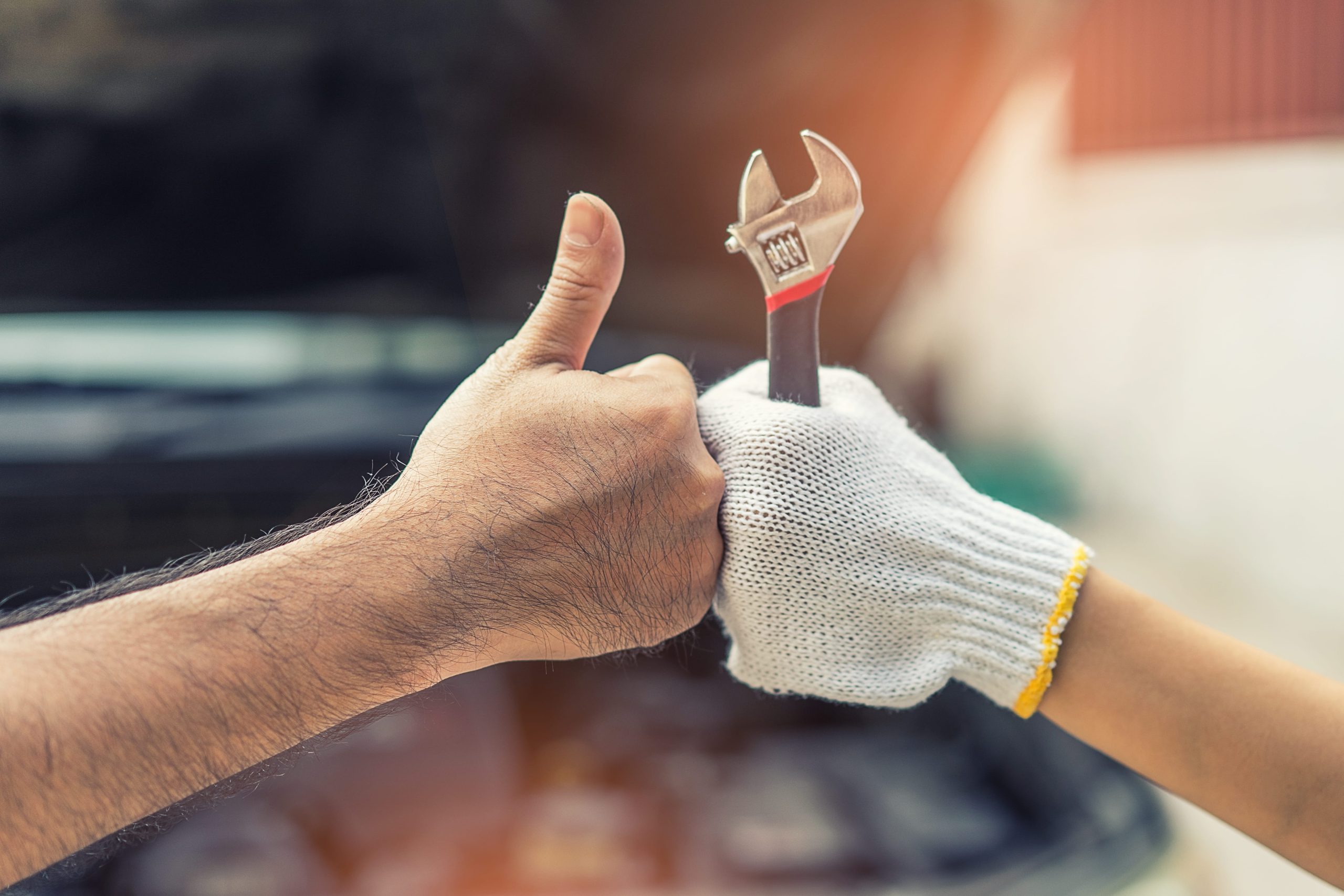 Close-up of a person giving a thumbs up next to a gloved hand holding a wrench
