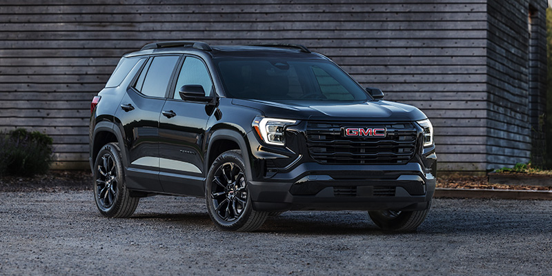 Black GMC Terrain parked on a gravel lot in front of a wooden building.