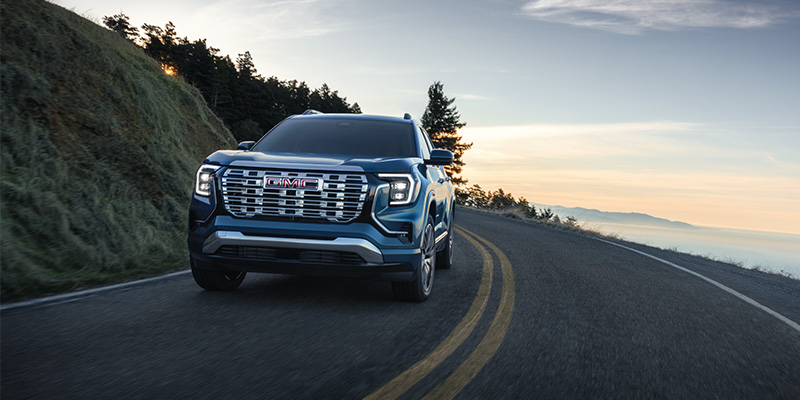 Blue GMC Yukon driving on a winding coastal road at sunrise.