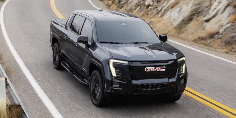Dark gray GMC Sierra EV pickup truck driving on a winding mountain road.